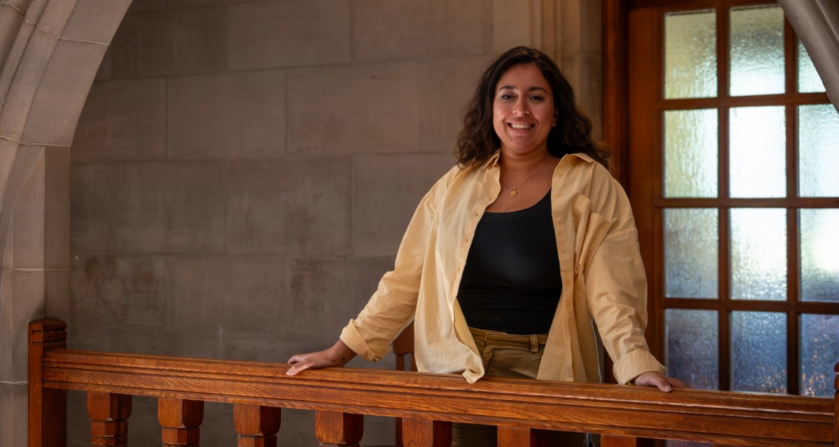 Fatima Qaraan standing in front of a balcony inside the Emmanuel College building.